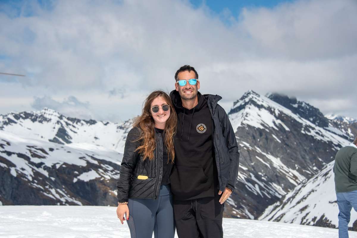 Couple standing on a glacier landing with snowy peaks behind, Glacier Jet trip from Wanaka