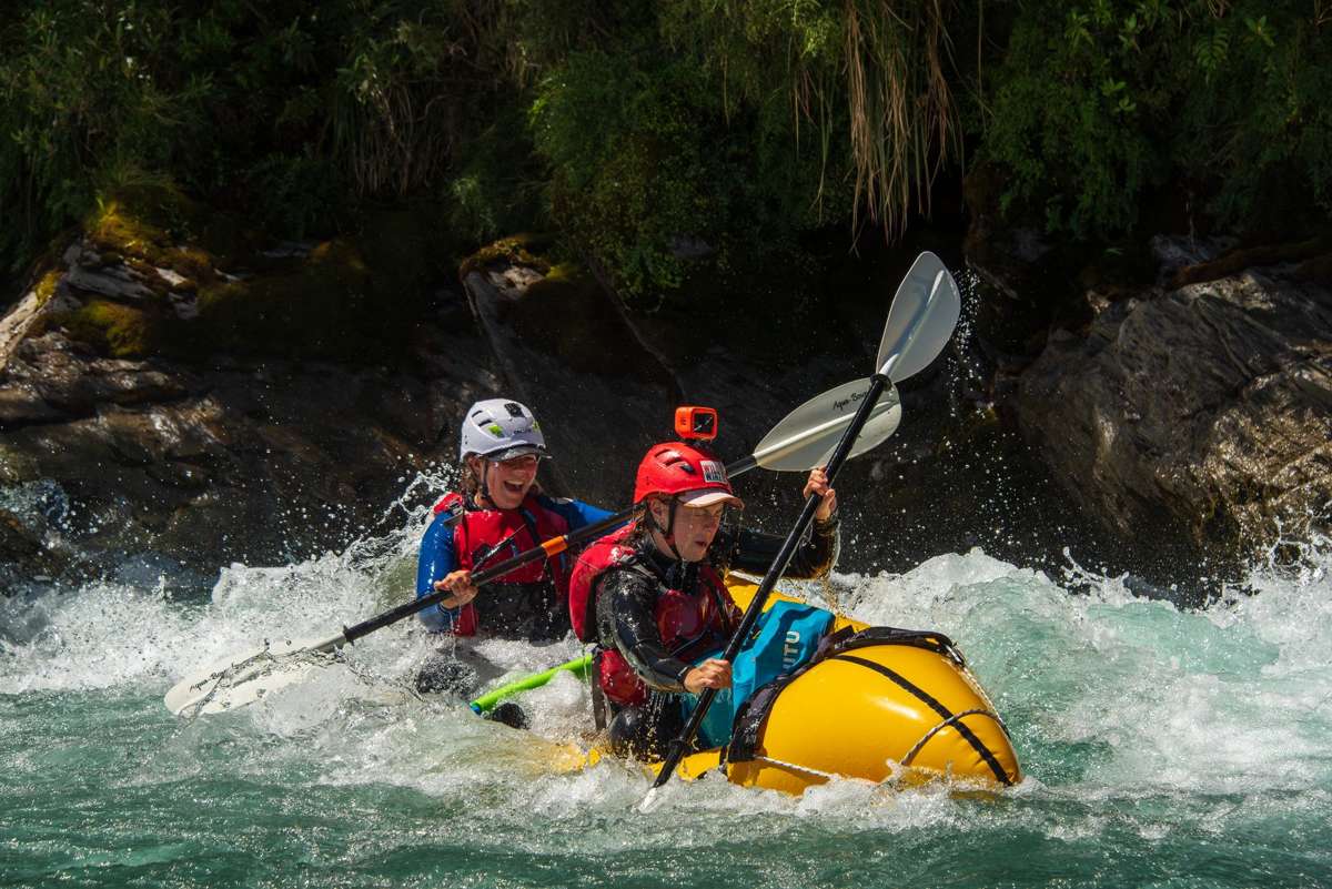 Packraft crew mid-rapid with paddles up